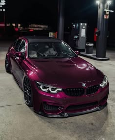 a purple car is parked in front of a gas station at night with its lights on