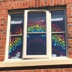 a rainbow painted on the side of a brick building with two windows that have hearts drawn on them