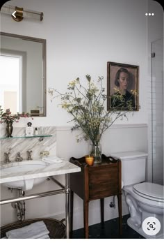 a bathroom with a sink, toilet and painting on the wall next to it's mirror