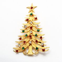 "DESCRIPTION: This exquisite vintage designer brooch by Mylu, dating back to the 1960s, is a captivating representation of holiday elegance. The Christmas tree motif, crafted from a lustrous gold-tone metal base with textured finishing, is adorned with a harmonious blend of red, green, and crystal rhinestones that glisten with festive allure. In impeccable mint condition and marked with the signature \"MYLU,\" this brooch measures a graceful 2.5\" in length, making it a timeless and cherished ac Designer Brooch, Gold Tree, Christmas Pins, Vintage Designer, Gold Texture, Safety Pin, Metal Base, Gold Tone Metal, Crystal Rhinestone