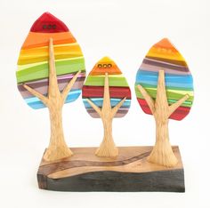 three wooden trees with multi - colored stripes painted on them, standing on a piece of wood