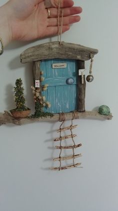 a hand is holding a miniature house made out of branches and twigs with a blue door