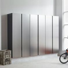 a bike parked next to a tall metal cabinet in front of a window with two boxes on the floor