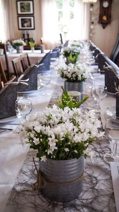 a long table with white flowers in buckets on it's centerpieces