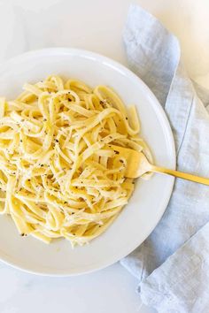 a white plate topped with pasta on top of a blue and white cloth next to a wooden spoon