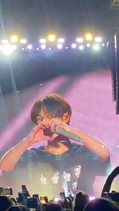 a man standing on top of a stage holding a microphone to his mouth and making a heart sign