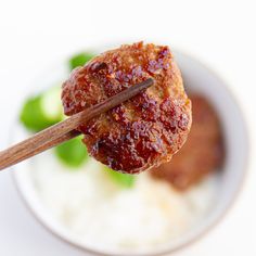 chopsticks sticking out of meat in a bowl with rice and green peppers on the side