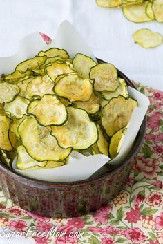 a bowl filled with sliced cucumbers on top of a floral table cloth next to a white towel