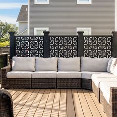 a couch and chair on a wooden deck near a house with grey siding, black iron fence and white cushions