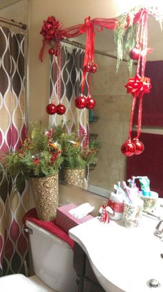 a bathroom decorated for christmas with red ornaments hanging from the ceiling and potted plants on the toilet