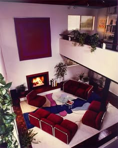 a living room with red couches and a fire place in the corner, surrounded by plants