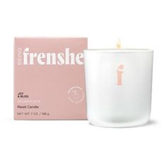 a white candle sitting next to a pink box on a white surface with the letter f in it