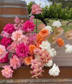 pink and white flowers sitting on top of a wooden bench in front of a barrel