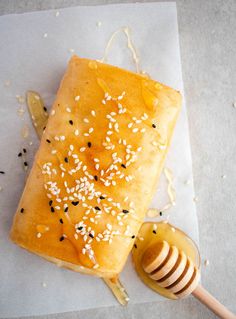 a piece of bread with sesame seeds on it next to a honey dipper and spoon