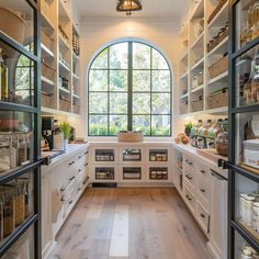 a kitchen with lots of white cupboards and open shelves in front of a large window