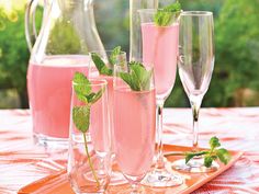 three glasses filled with pink liquid and mint sprigs on a tray next to two pitchers