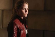 a woman in a red leather jacket looks off into the distance while standing against a wall