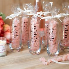 pink candies in clear glass vases with white ribbon on table next to flowers