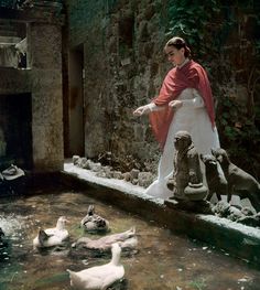 a woman standing in front of a fountain filled with ducks