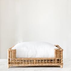 a wicker bed with white linens and pillows on the bottom, in front of a wall