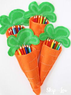 two carrot shaped pencils with green leaves on them and colored pencils in the middle