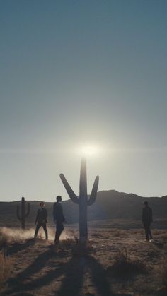 three people are walking in the desert near a cactus and a large saguado