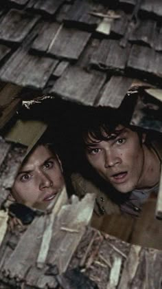 two people standing in front of a pile of wooden planks looking at the camera