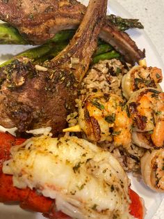 a white plate topped with meat, shrimp and veggies next to asparagus