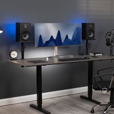 a computer desk with speakers and a monitor on it in front of a gray wall