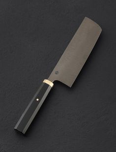 a large knife on a black surface with a gold handle that matches the rest of the blade