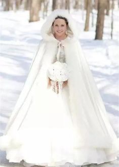 a woman in a white wedding gown and fur stole holding a bouquet standing in the snow