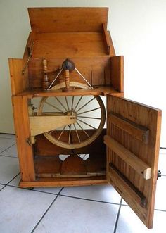 an old spinning wheel in a wooden box on the floor next to a white wall