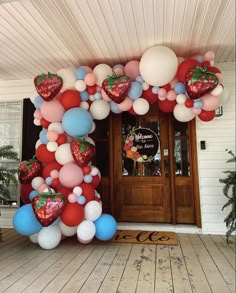 a bunch of balloons that are on the front of a house with strawberries and heart shaped balloons