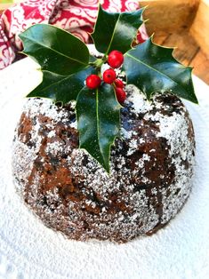 a white plate topped with a pastry covered in powdered sugar and holly leaf decorations