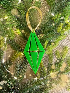 a green origami christmas ornament hanging from a pine tree with lights in the background