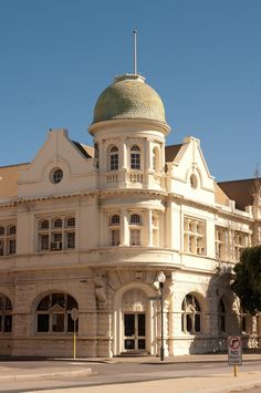 an old white building with a green dome on the top and two stories below it