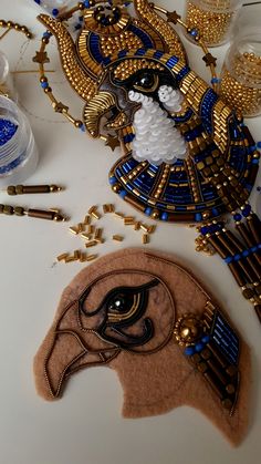 an egyptian mask and other decorative items on a counter top with beads, glass bottles and gold trimmings