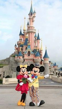 mickey and minnie mouse standing in front of a castle