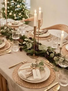 the table is set for christmas dinner with candles and greenery on each place setting