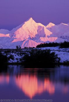 the snow covered mountains are reflected in the still water at sunset, with purple hues