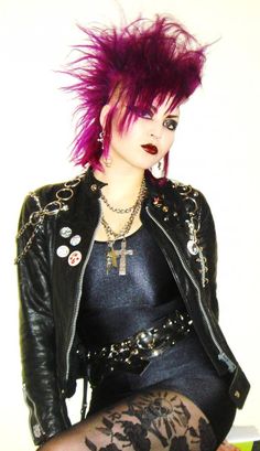 a woman with pink hair sitting on top of a wooden table wearing a black leather jacket