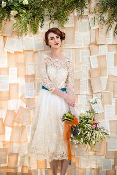 a woman standing in front of a wall with books on it and holding a bouquet