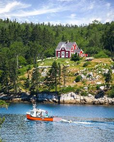 a boat traveling on the water in front of a red house