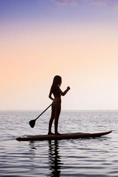 a woman standing on top of a surfboard in the ocean with a oar