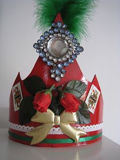 a red hat with green feathers and flowers on the top is adorned with brooches