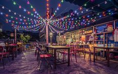 an outdoor dining area with colorful lights strung across the ceiling and tables, chairs, and bookshelves