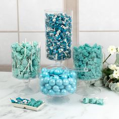 blue and white candies in clear containers on a marble counter with flowers behind them