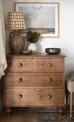 a wooden dresser with two vases and a lamp on top of it next to a painting