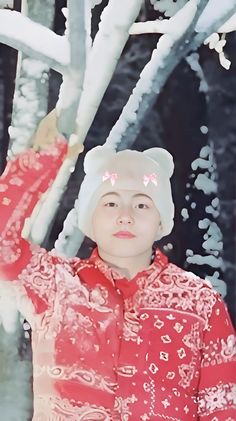 a woman in a red shirt and white hat standing next to a tree with snow on it