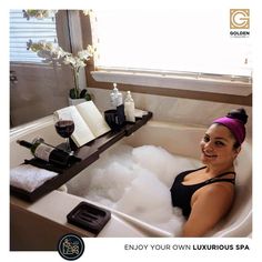 a woman sitting in a bathtub filled with foam next to a bottle of wine